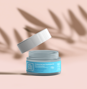 Pot de crème de jour hydratante Alcedo ouvert, couvercle en suspension au-dessus du pot, sur fond beige.