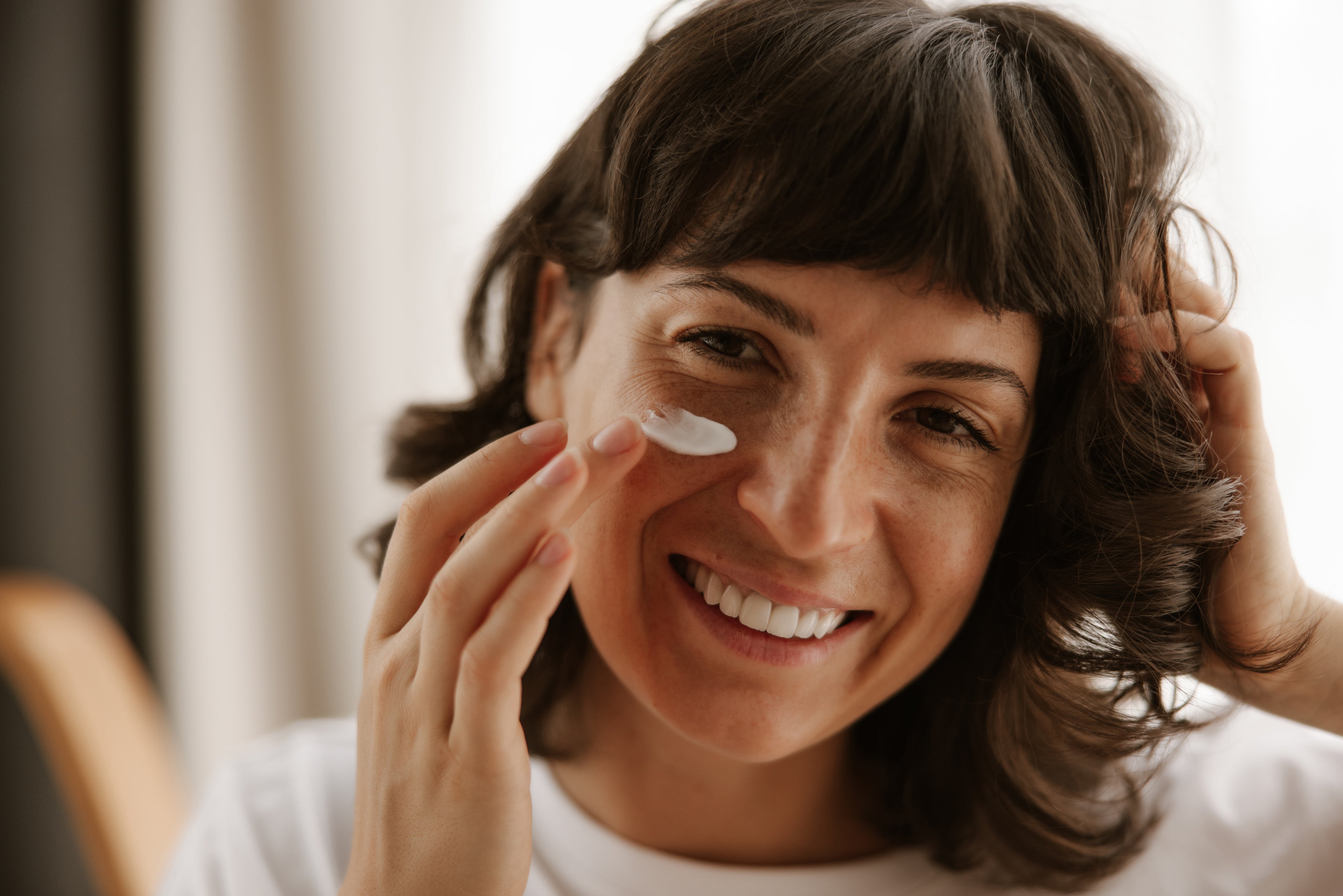 close-up-view-happy-woman-products-skin-cream-looking-mirror.jpg
